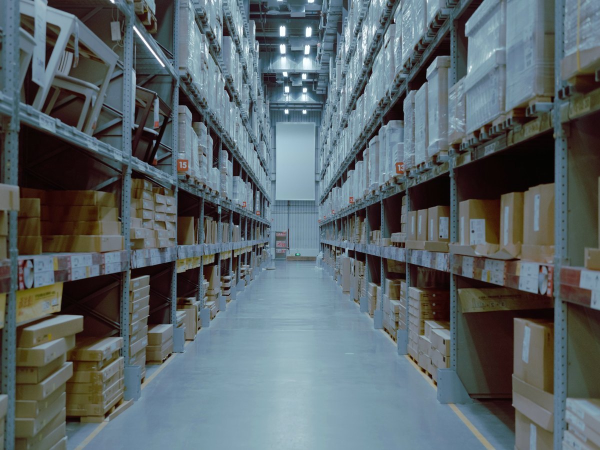 A long aisle of racked stock in a bright distribution warehouse